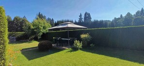 A covered outdoor seating area with a table and chairs, surrounded by a well-maintained lawn and hedges.