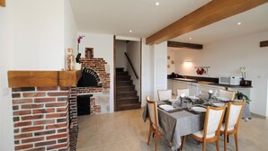 Un coin repas agrémenté d’une cheminée en briques, un escalier menant à une autre pièce et une cuisine équipée d’appareils électroménagers modernes.