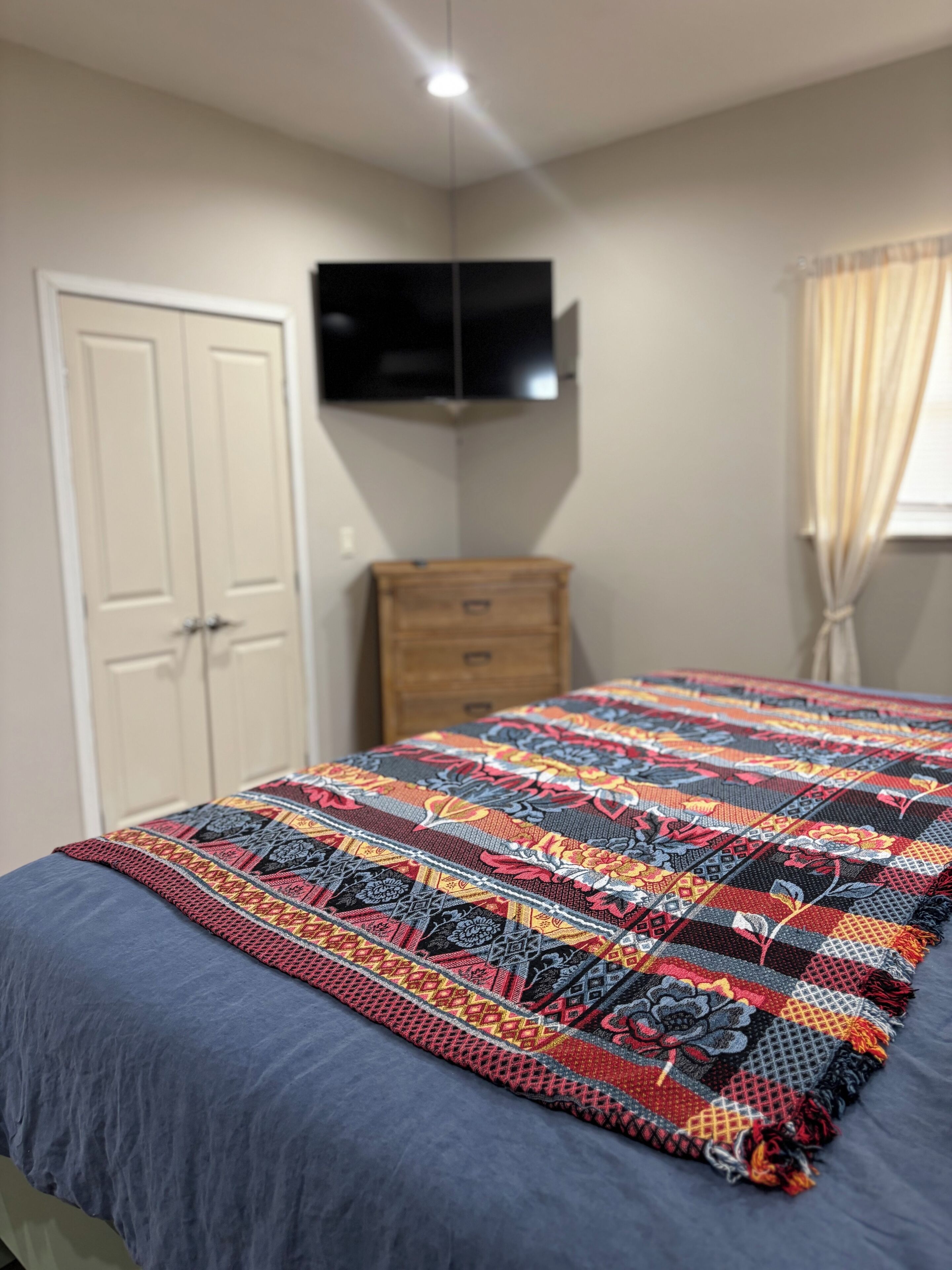 A bedroom with a bed, a TV mounted on the wall, a wardrobe, and a window with curtains.