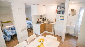 A compact kitchenette with a gas stove, sink, and a microwave. There is a dining table with a plate of food and a bottle of wine.
