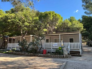 Two mobile homes with white railings, surrounded by trees and a gravel driveway.