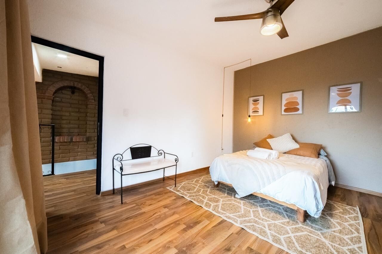 A bedroom with a bed, a bench, a brick wall, and a ceiling fan.