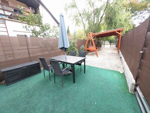 Une terrasse avec une table et des chaises, une balançoire et un espace abrité avec un parasol.
