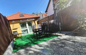Un espace extérieur aménagé avec une table et des chaises, un petit coin salon couvert et un tuyau d’arrosage pour le jardin.