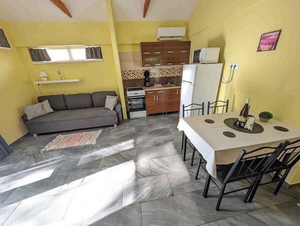 Un espace de vie compact comprenant un canapé, une table à manger, un coin cuisine et une petite fenêtre.