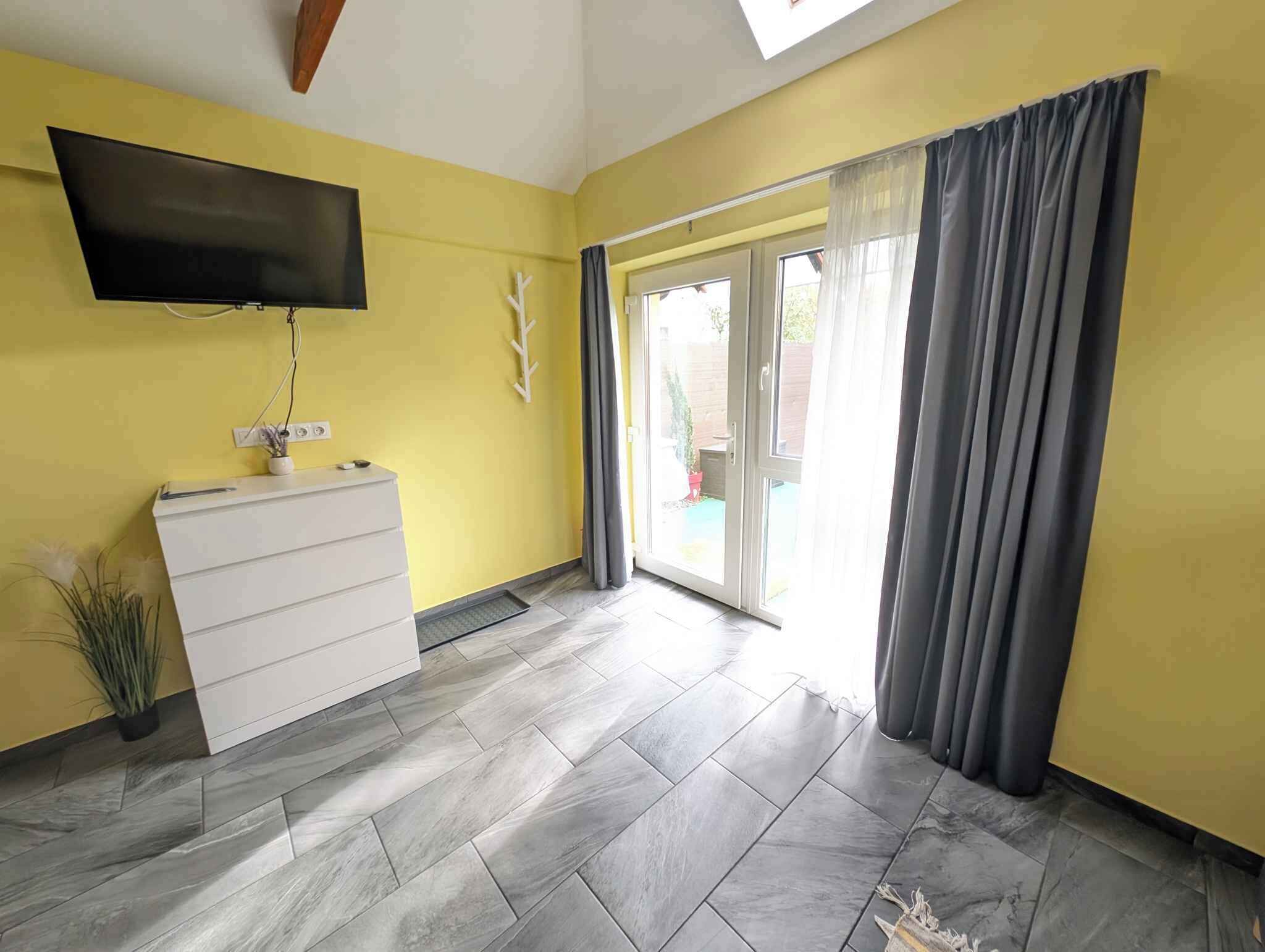 Una habitación con un aparador blanco, un televisor de pantalla plana montado en la pared y un armario corredero que da a un espacio al aire libre.