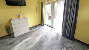 A room with a white dresser, a flat-screen TV mounted on the wall, and a sliding glass door leading to an outdoor area.
