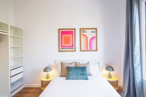 Une chambre d’hôtel comprenant un lit, deux tables de chevet avec des lampes, une armoire et deux œuvres d’art encadrées accrochées au mur.