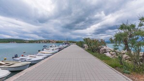 Un paseo marítimo con una fila de barcos amarrados a la izquierda y un camino pavimentado que conduce al agua.