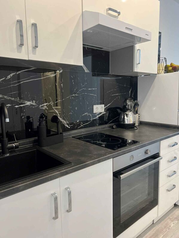 A modern kitchen with white cabinets, a black marble backsplash, stainless steel appliances, and a built-in oven.