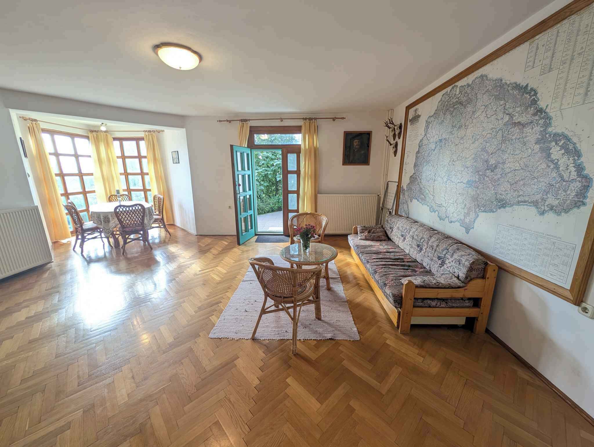A spacious living room with a wooden herringbone floor, a round table with chairs, a sofa, and a large map on the wall.