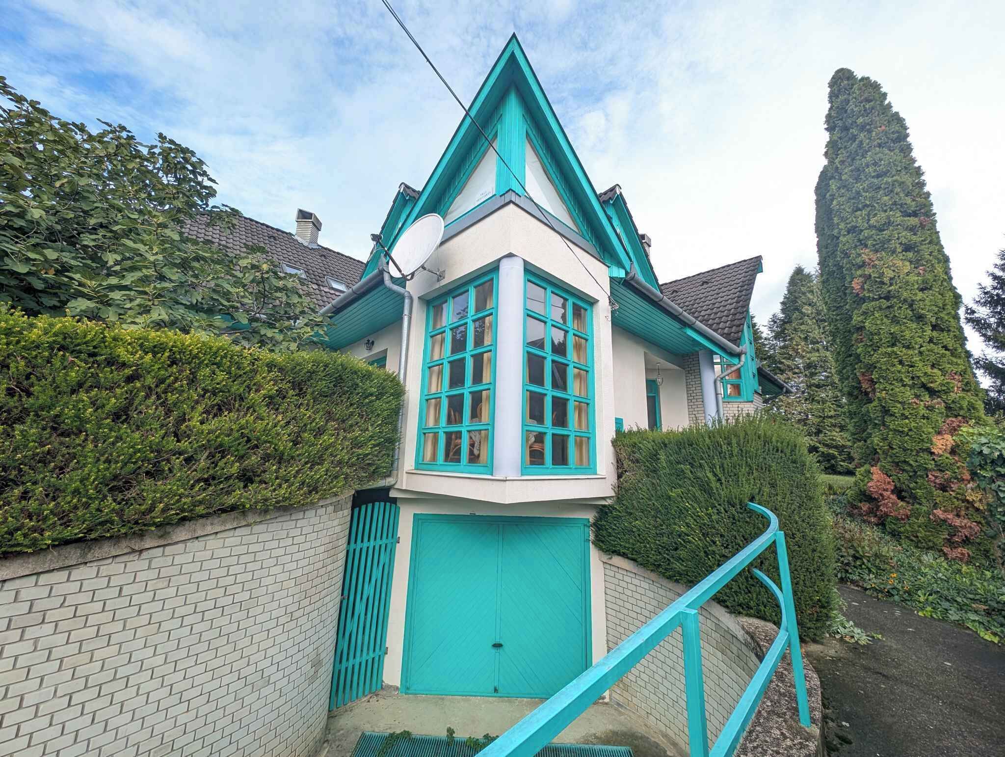 A house with a distinctive corner turret, a brick wall, and a green gate.
