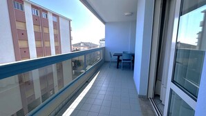 A balcony with a glass railing, a table, and chairs. - Holiday apartment with pool near the sea (Bibione)