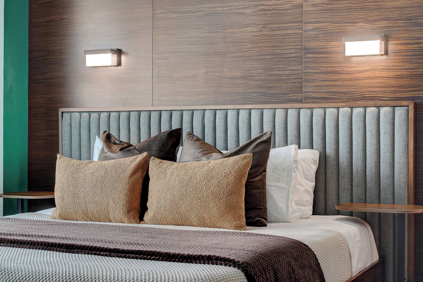 A modern hotel room with a large bed, a padded headboard, and two bedside tables.