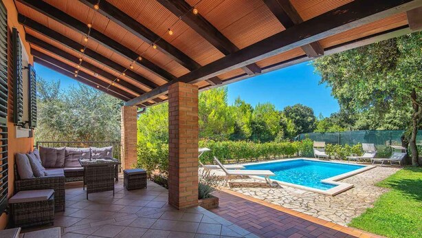 An outdoor patio with a pool, wicker furniture, and a brick pillar.