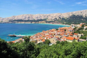 Un pueblo costero con edificios, un puerto deportivo y montañas al fondo.