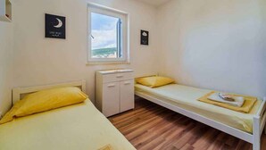 Eine kleine Einzelunterkunft mit einem Bett, einem kleinen Schrank und einem Fenster mit Blick auf das Meer.
