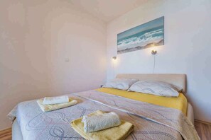 A bedroom with a bed, pillows, and a painting of a beach scene. - Holiday flat with balcony (Punat)