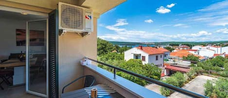 A balcony with a table and chairs, an air conditioning unit, and a view of a town with red-roofed houses.