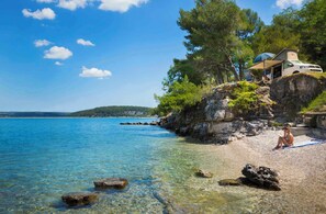 A beach with clear water, a rocky shore, and a white van with a canopy on a cliff. - Mobile home with air conditioning and terrace with sea view (Tar/Poreč)