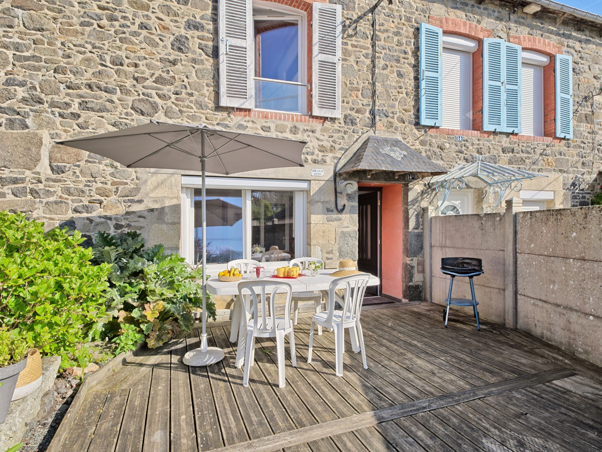 A stone building with a wooden deck, outdoor seating, and a grill.
