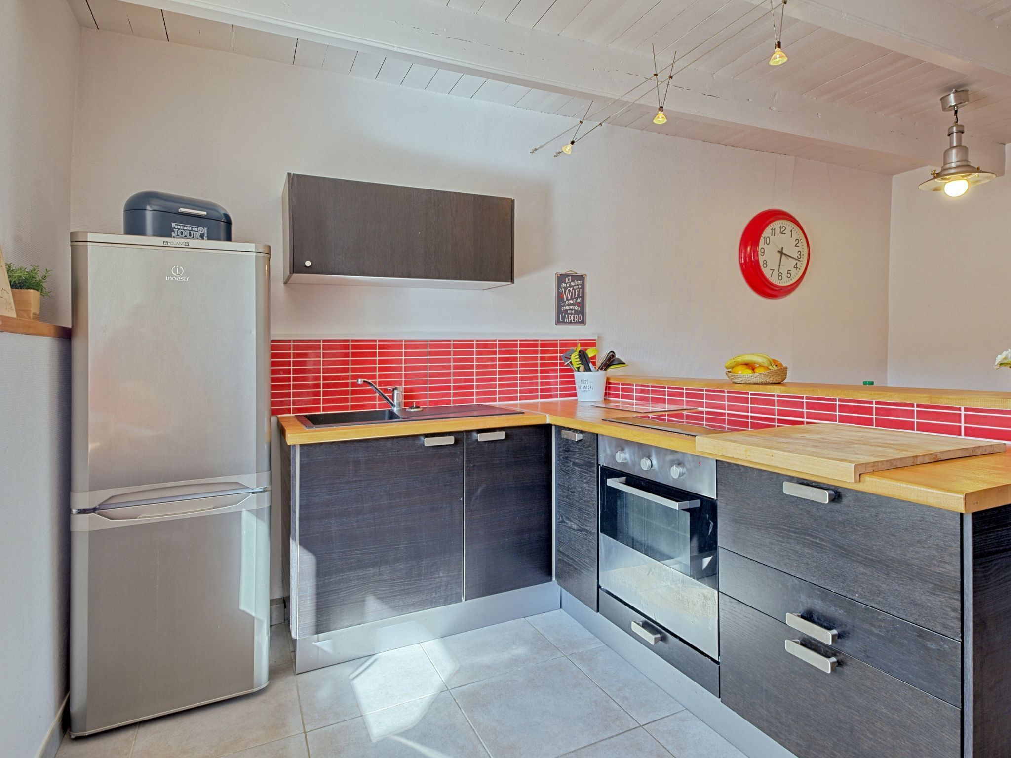 Eine moderne Küche mit einem Edelstahl-Kühlschrank, einem Einbauofen und einer roten Küchenrückwand.