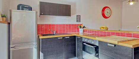 Eine moderne Küche mit einem Edelstahl-Kühlschrank, einem Einbauofen und einer roten Küchenrückwand.