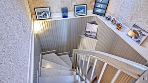 A staircase with a white railing, leading to a landing with a shelf displaying framed photographs and a small model ship.