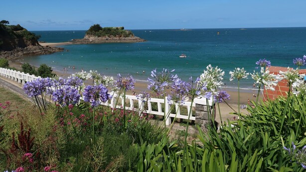 A coastal view with a white fence, beach, and rocky outcrop.