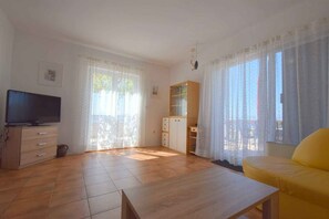 Una sala de estar con televisión, muebles de madera, un sofá y un balcón con cortinas.