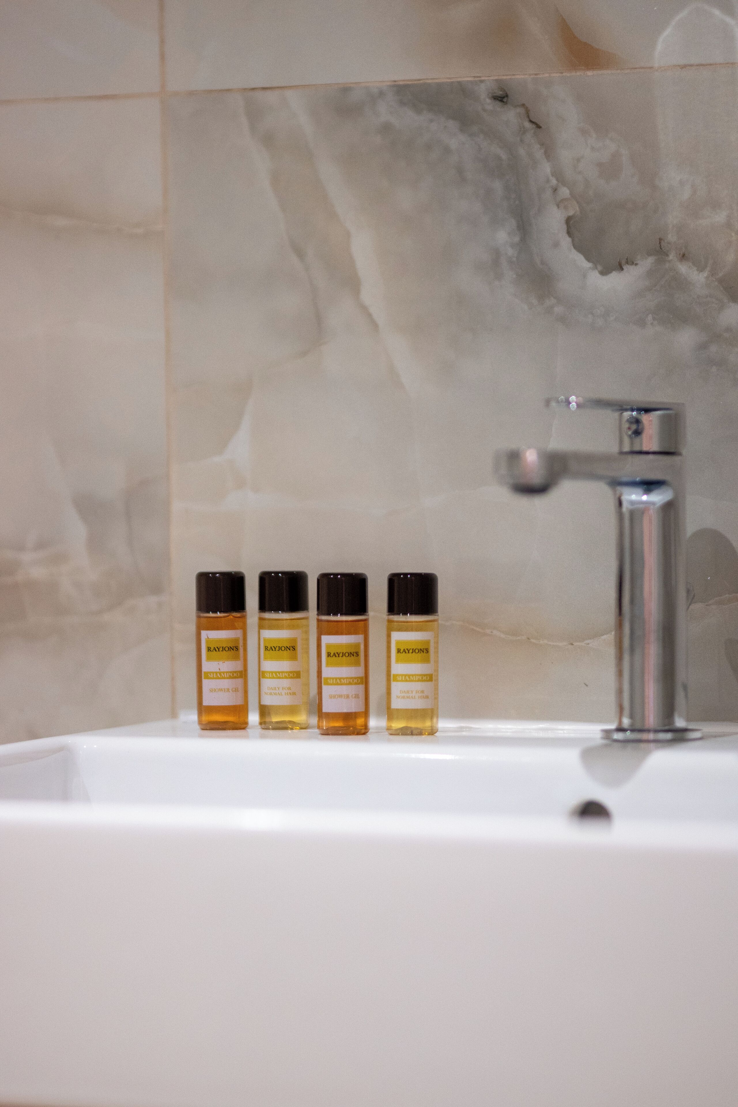 A bathroom with a white sink, three bottles of shampoo, and a chrome faucet.