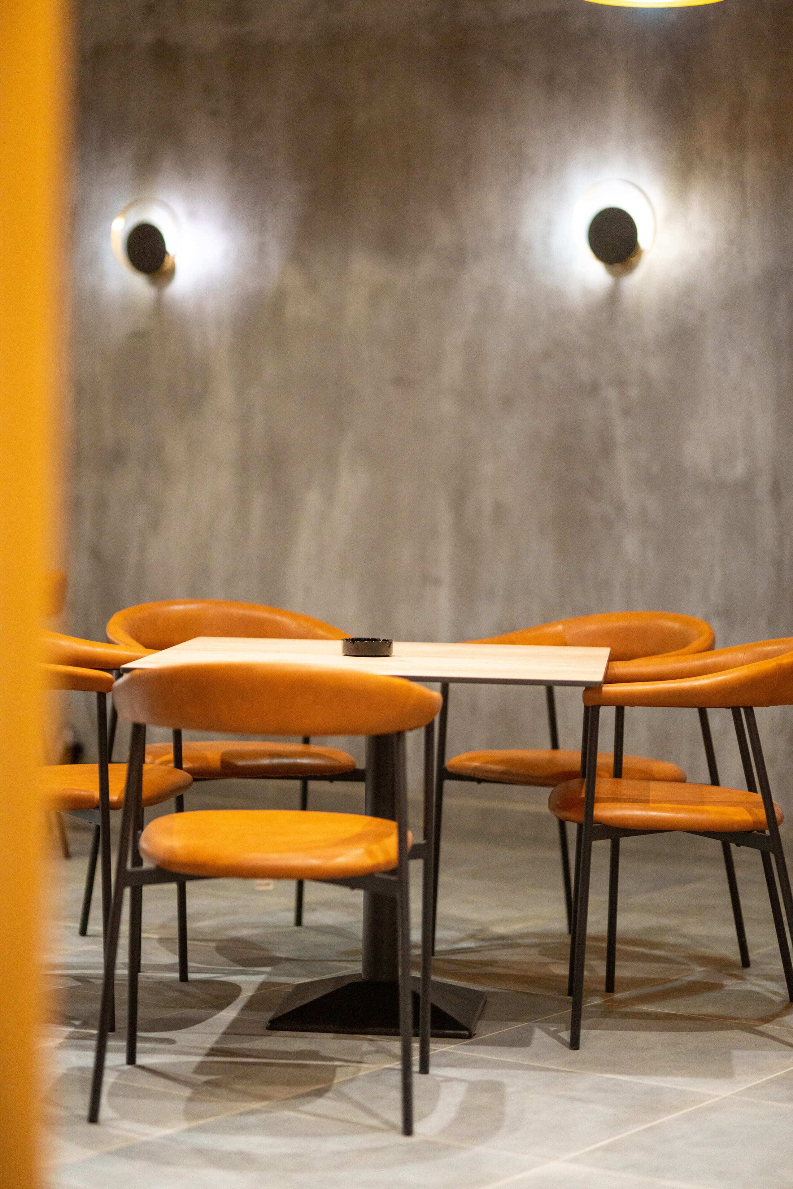 Een eethoek met een ronde tafel en oranje stoelen, een lamp aan de muur en een vloer met patroon.