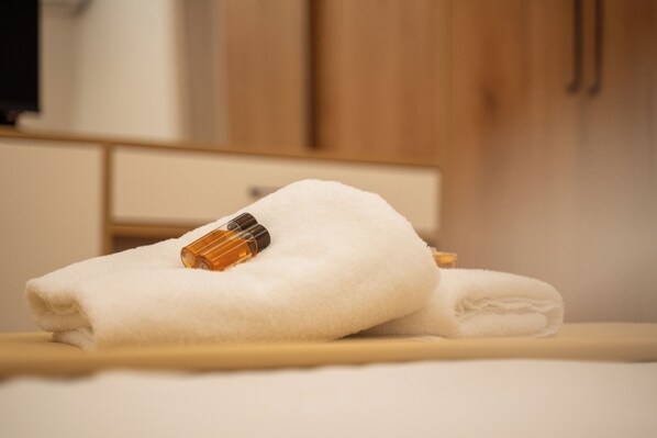 A neatly folded white towel on a wooden surface with a bottle of lotion. - iLLYRIA HOTEL (Ulcinj)