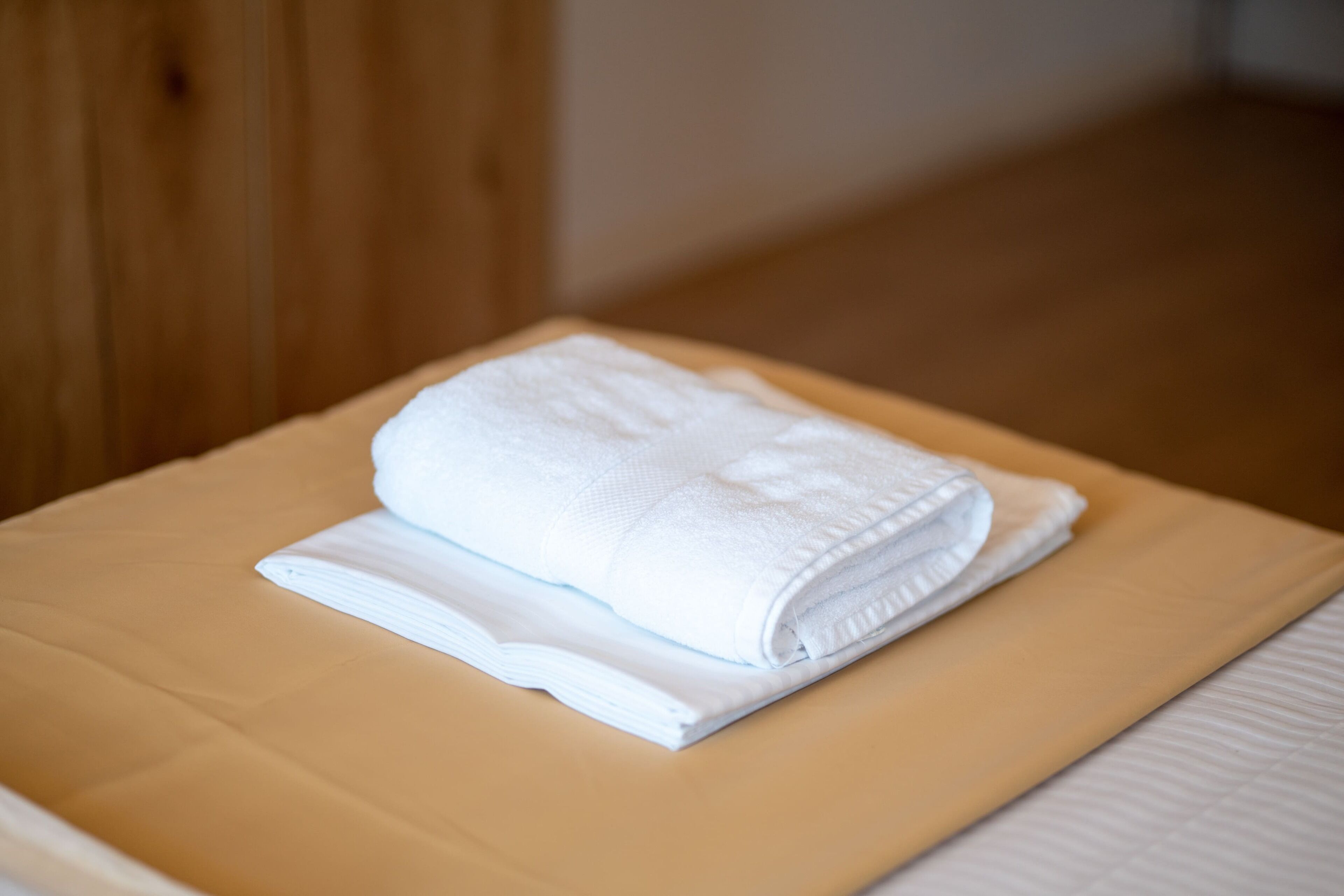 A neatly folded white towel on a beige bed in a hotel room.