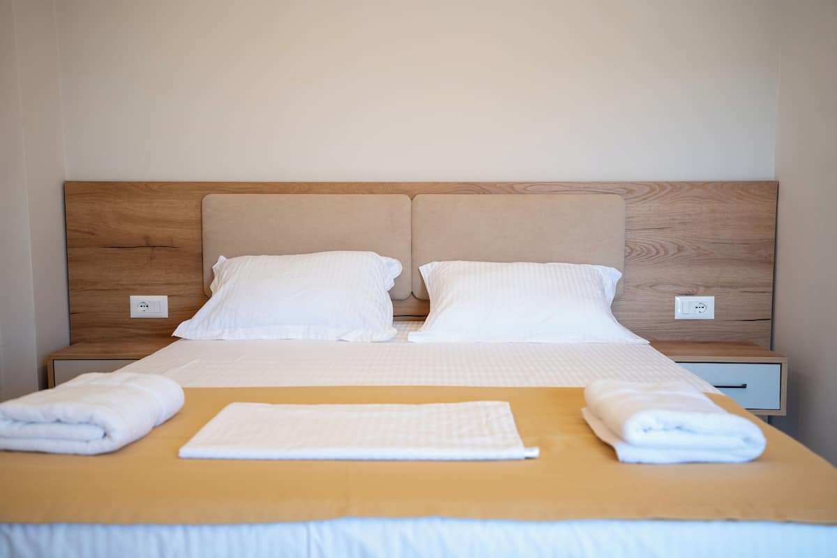 Un letto matrimoniale rifatto con cura, dotato di una testiera in legno, due cuscini bianchi e un asciugamano bianco piegato.