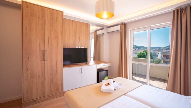 A hotel room with a bed, a TV, a wardrobe, and a balcony with a city view. - iLLYRIA HOTEL (Ulcinj)