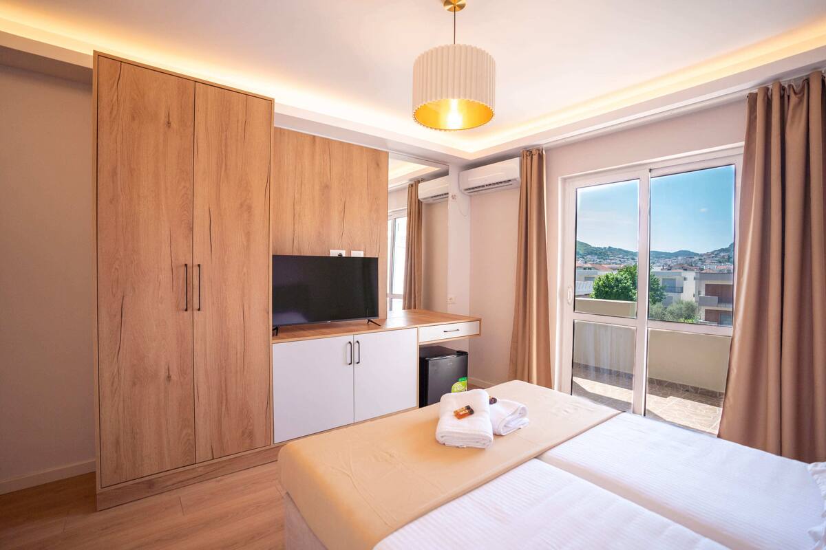 Una camera d'albergo con un letto, una TV, un armadio e un balcone vista città.