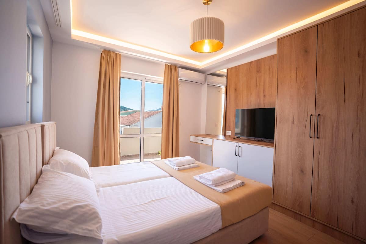 Camera d'albergo con due letti, una TV, armadietti in legno e vista sull'esterno.