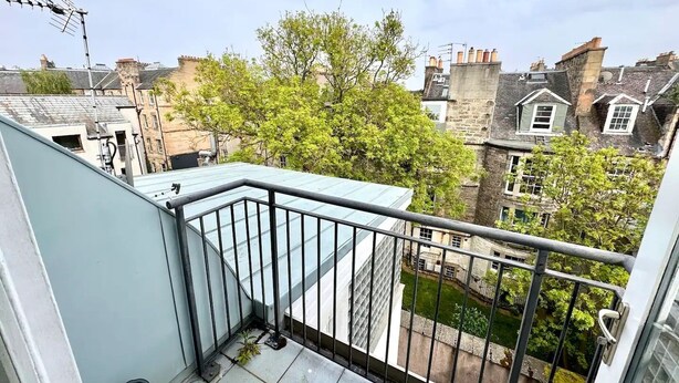 A balcony with a metal railing, a small potted plant, and a view of surrounding buildings and trees. - Convenient Edinburgh City Centre 2 Rooms + Parking (Edinburgh)