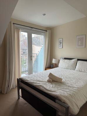Un dormitorio con cama, cortinas, una ventana y una lámpara fijada a la pared.