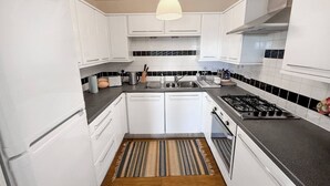 A modern kitchen with white cabinets, a gas stove, a sink, and a hanging light fixture. - Convenient Edinburgh City Centre 2 Rooms + Parking (Edinburgh)