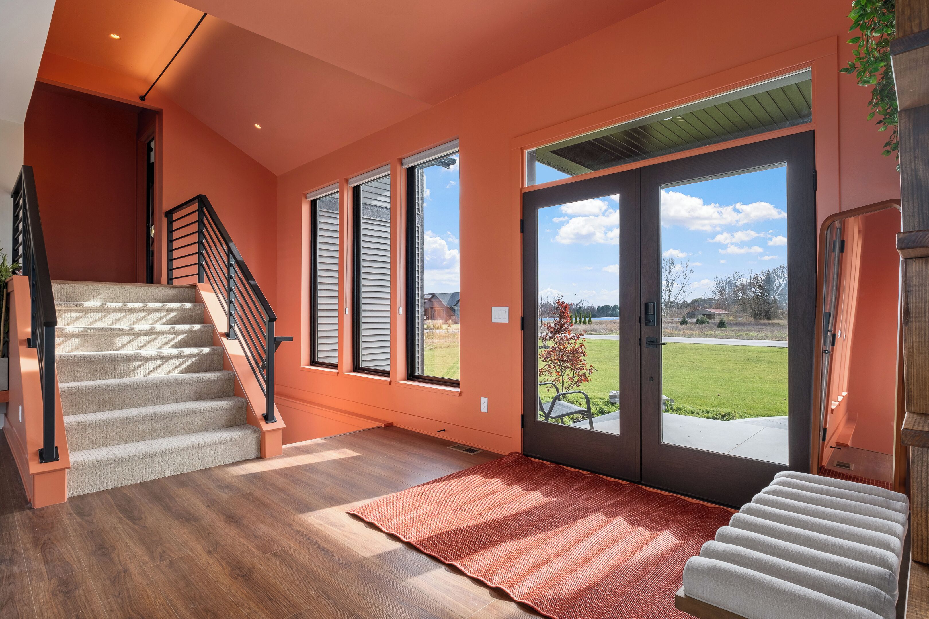 A spacious interior with a wooden staircase, large windows, and a view of the outdoors.
