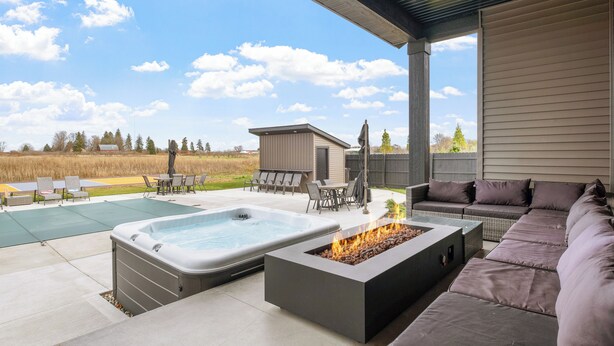 A covered outdoor patio with a hot tub, fire pit, and seating area. - 7bd 8bath Hot tub, Pool, Game Room, Sauna, Professional Pickleball Court (Fennville)