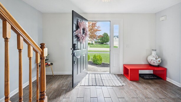 Un couloir avec un escalier en bois, un banc rouge et une porte donnant sur l’extérieur.