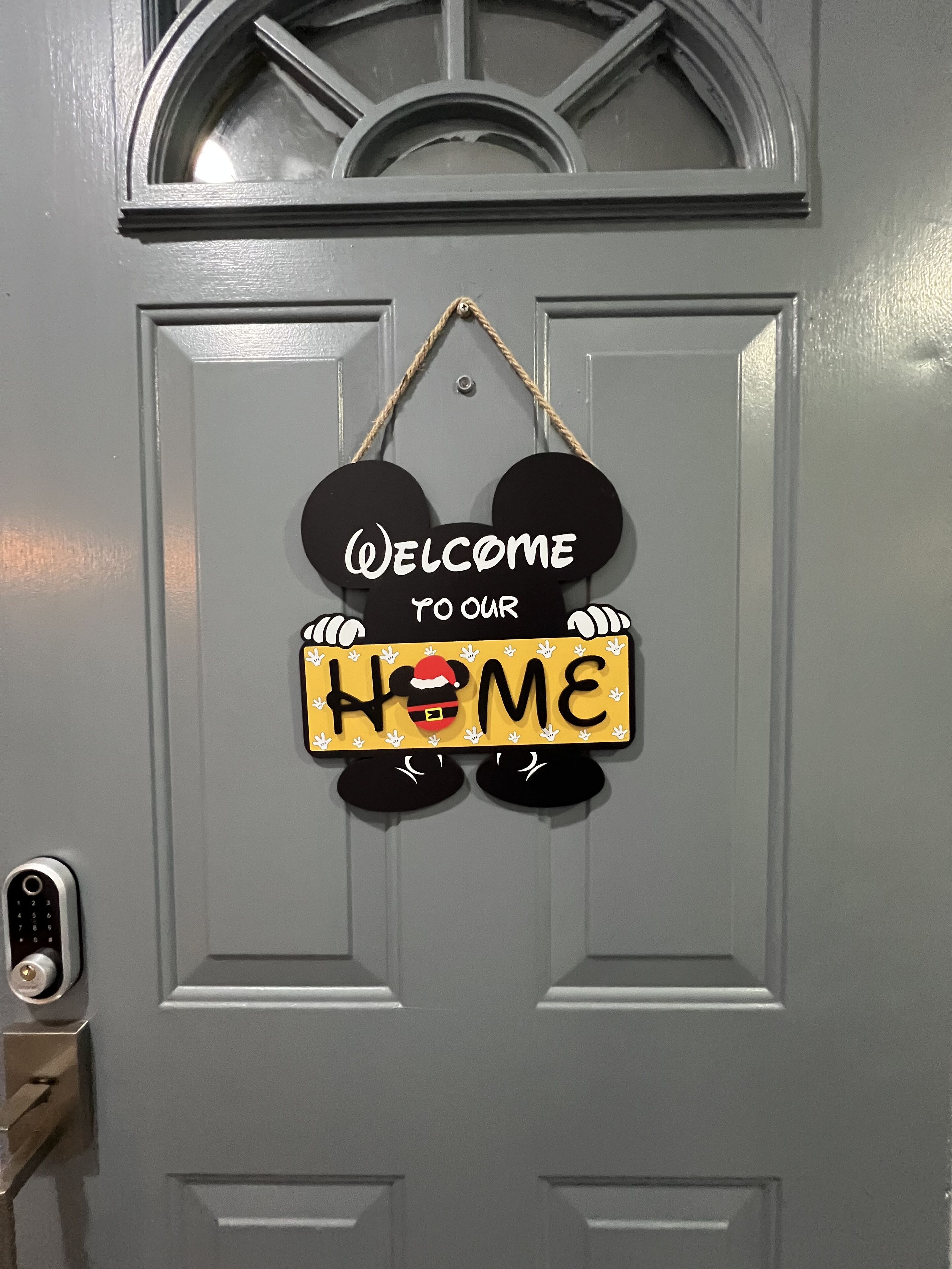 Une porte ornée d’une pancarte sur laquelle on peut lire « Bienvenue chez nous », avec des oreilles de Mickey Mouse et un bonnet du Père Noël.