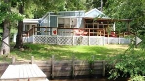 A cabin with a deck, surrounded by a wooden fence, near a body of water. - Hearts Cottage Waterfront Caddo Big Cypress River (Karnack)