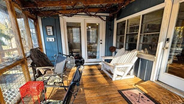 A covered porch with wooden flooring, a bicycle, and outdoor seating. - Hearts Cottage Waterfront Caddo Big Cypress River (Karnack)