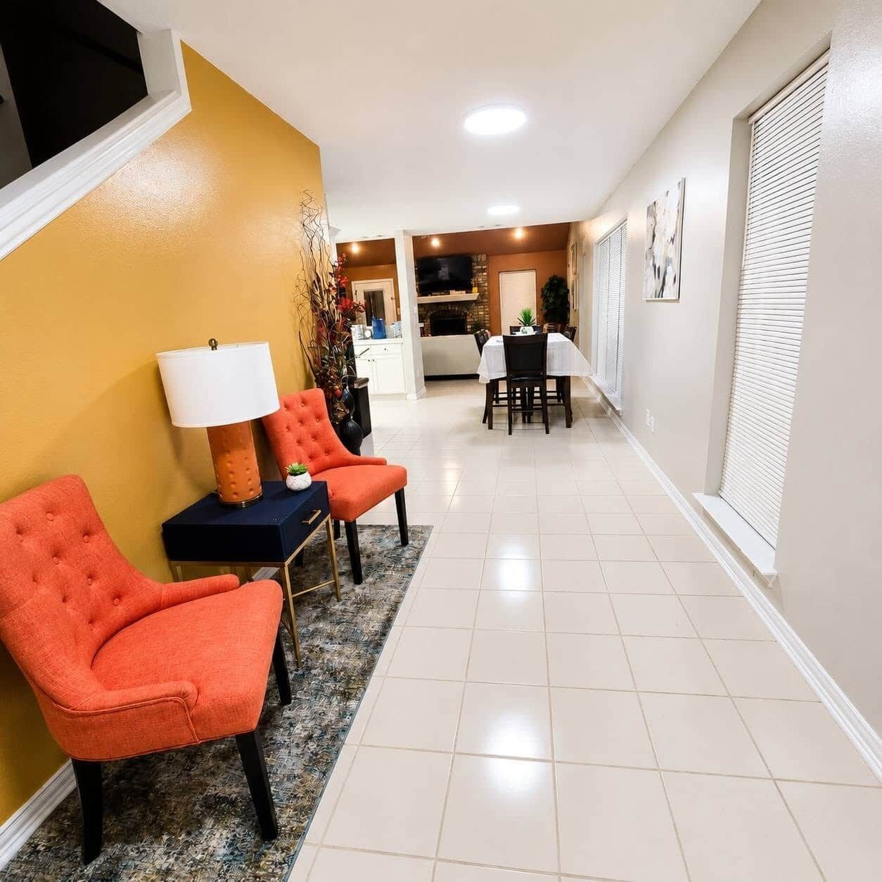 A hallway with a dining area, a kitchen, and a living room with orange chairs and a lamp.