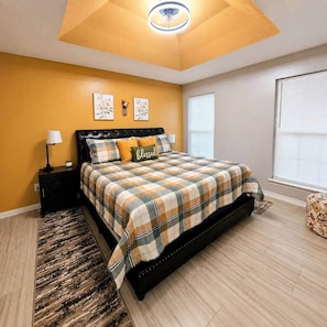 A bedroom with a bed, a nightstand, a lamp, a ceiling fan, and a window. - Rest A While Townhome (Tyler)