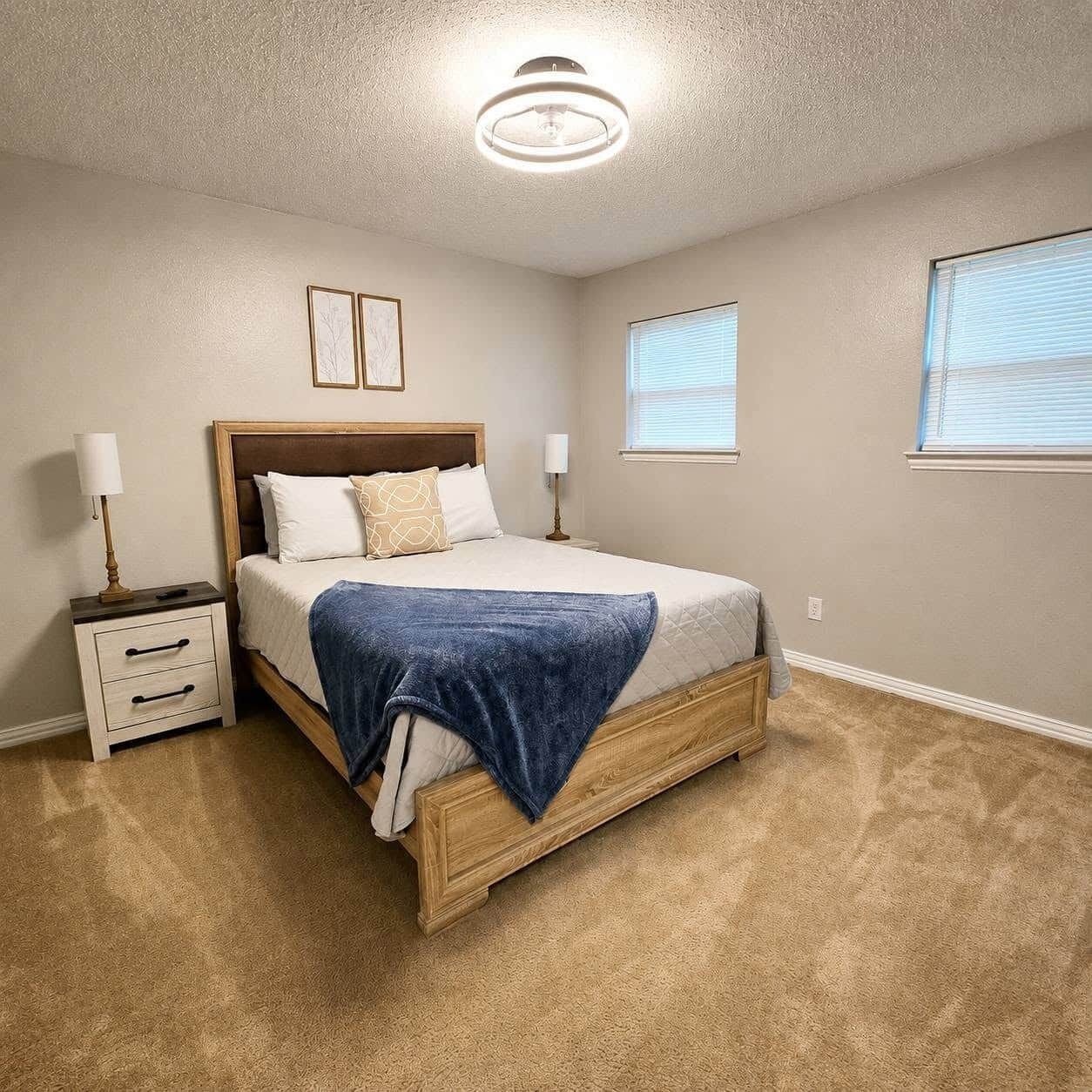 Une chambre à coucher avec un lit, des tables de chevet, un luminaire au plafond et deux fenêtres.